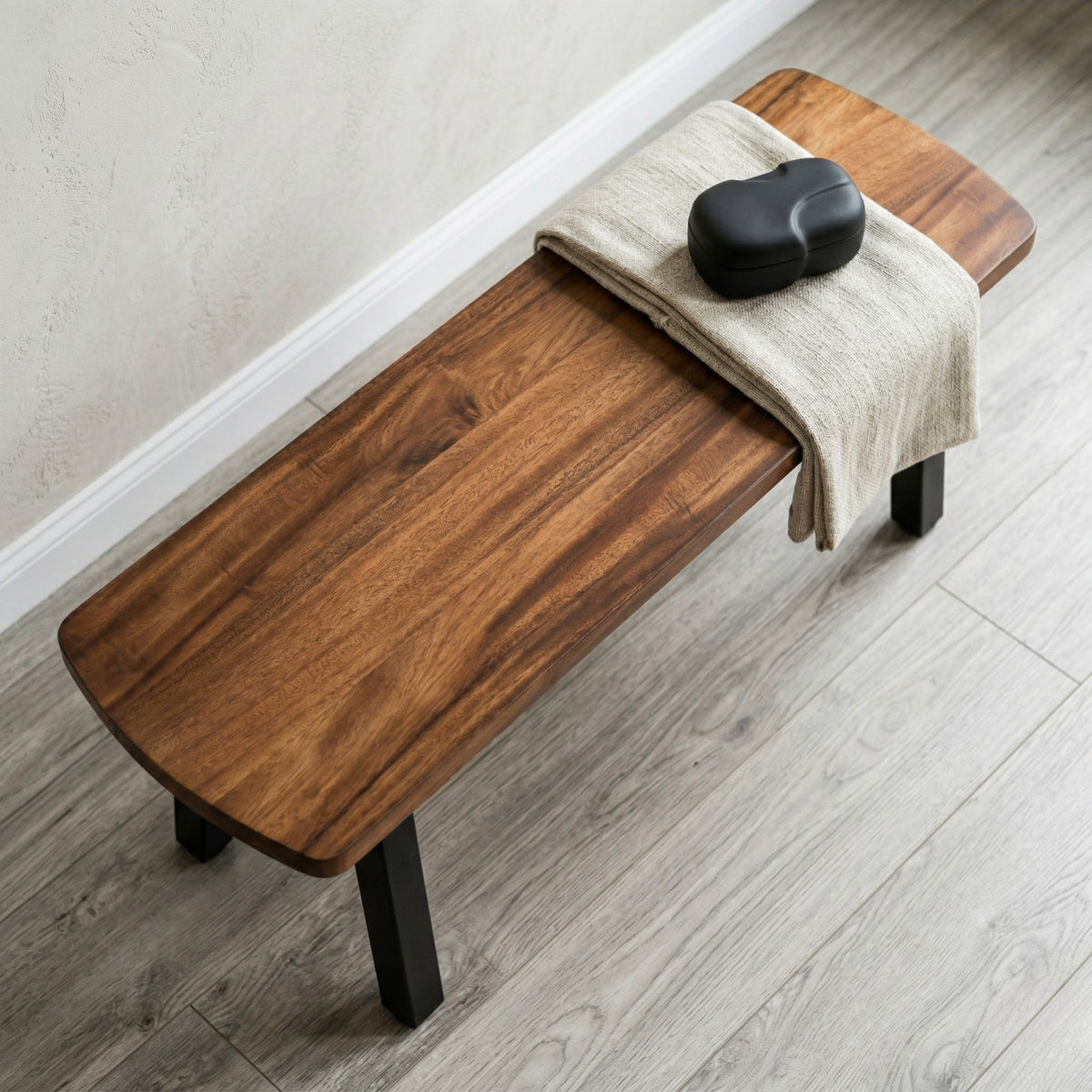 Wooden bench with a towel and black object on a wooden floor.