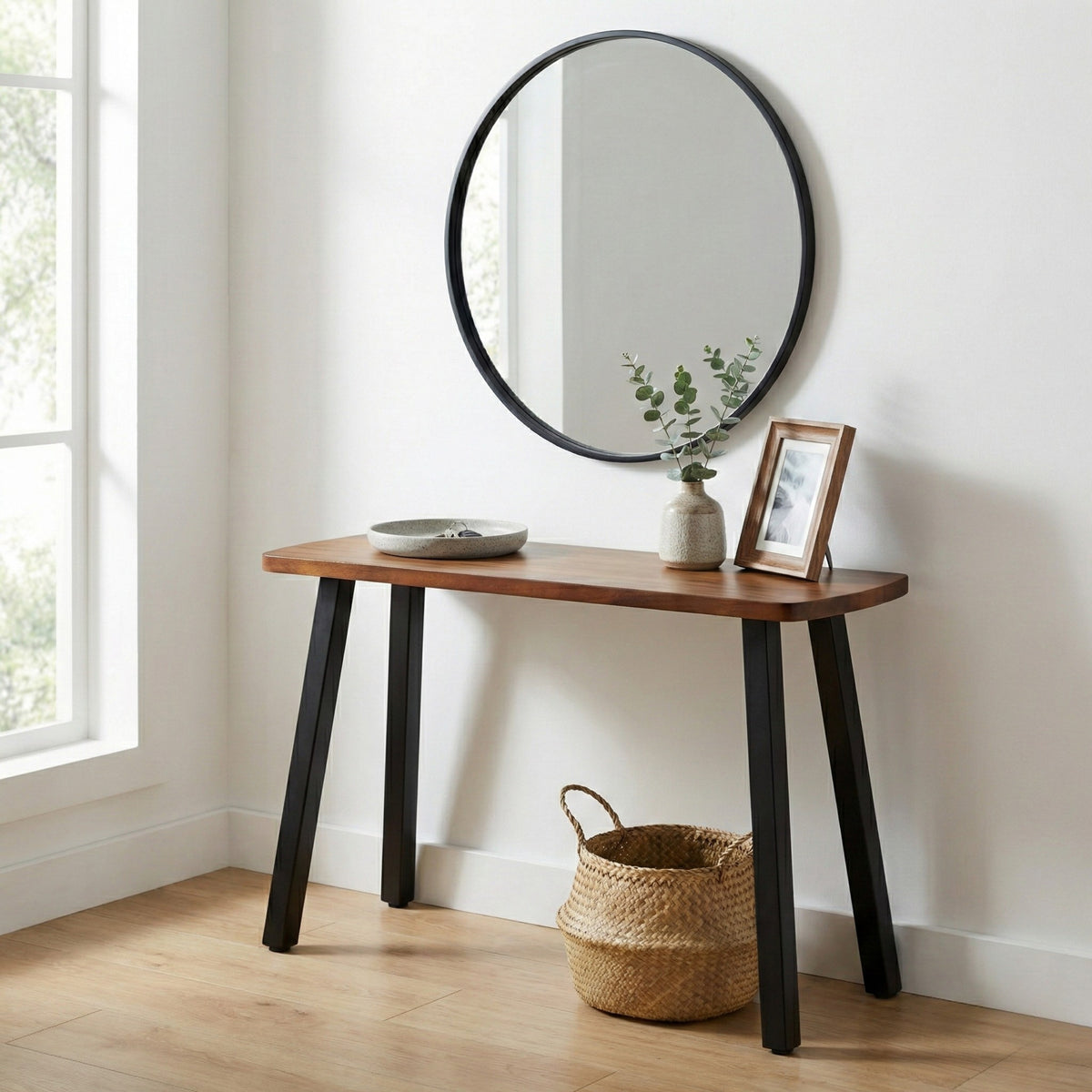 Walnut console table with round mirror, decorative items, and a basket in a bright room.