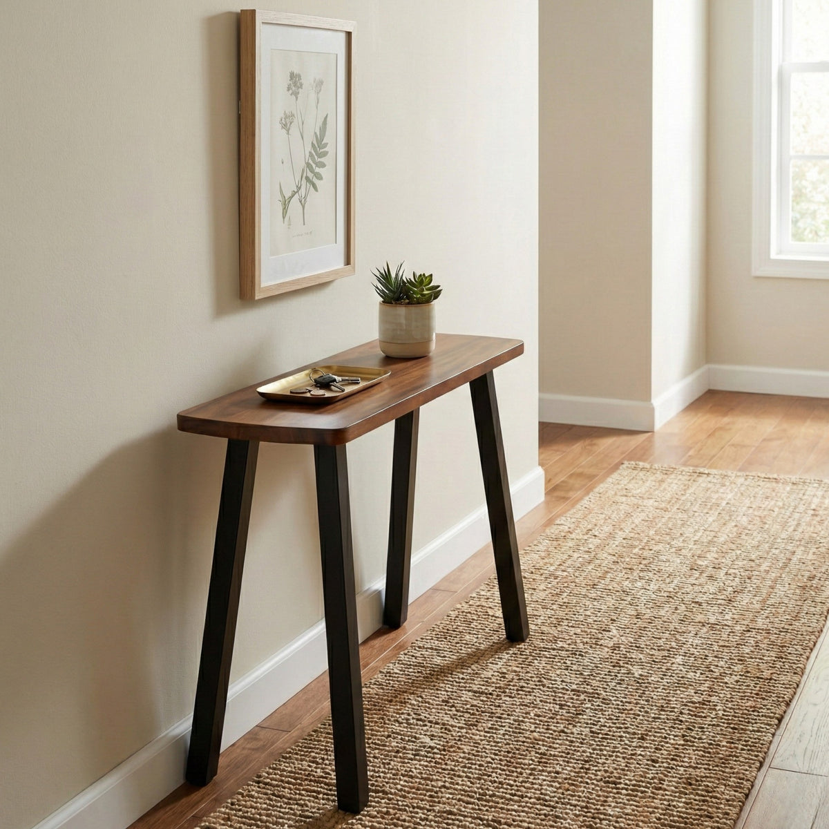 Wood console table with a plant and decorative items against a wall with a framed picture.
