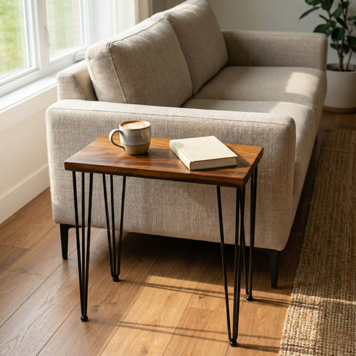 Walnut Side Table with a cup and book next to a beige sofa in a room with a window.