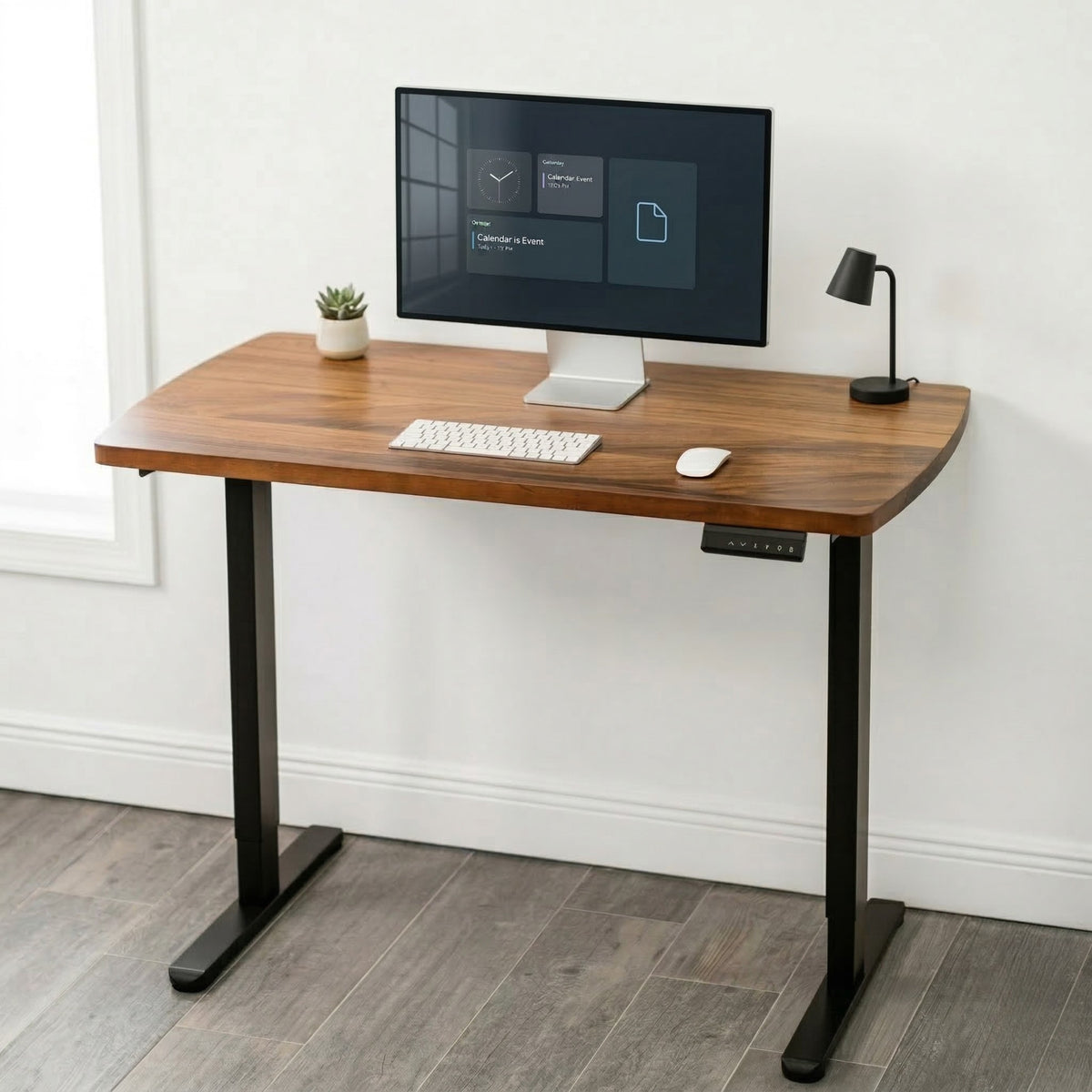 Narrow walnut standing desk with a computer setup against a white wall.