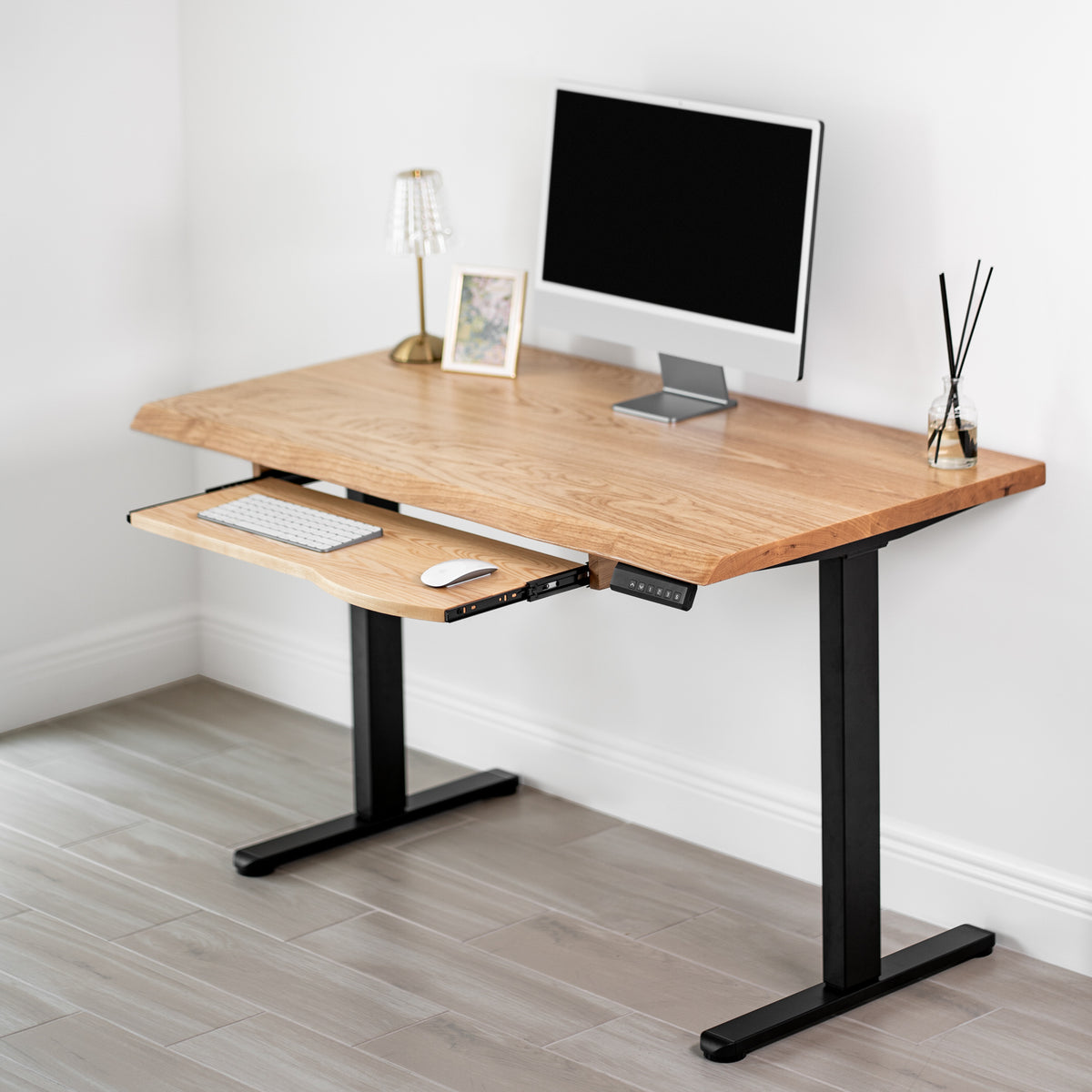 White oak standing desk with keyboard tray, black adjustable-height legs in a room setting