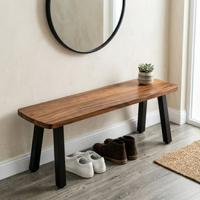 Solid wood entryway bench in a hallway with shoes and a plant on it, next to a round mirror.