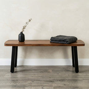 Walnut solid wood bench with black legs, a vase, and folded fabric against a neutral wall.