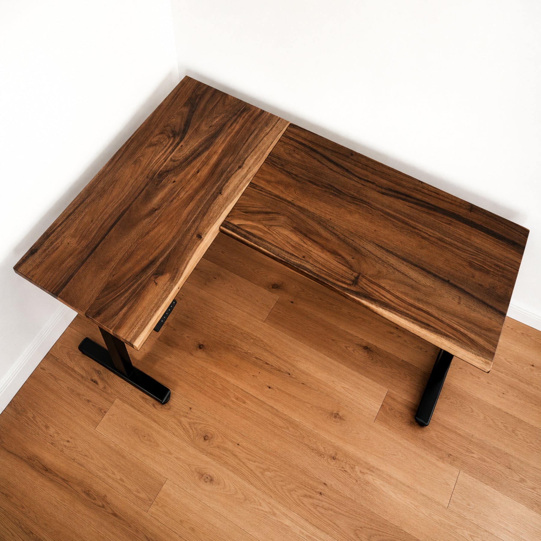 Walnut L-shaped standing desk with black legs on a wooden floor