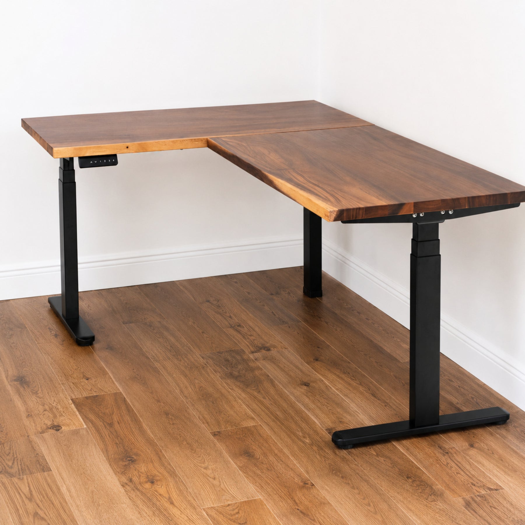 Walnut L-shaped standing desk with black adjustable legs on a wooden floor.