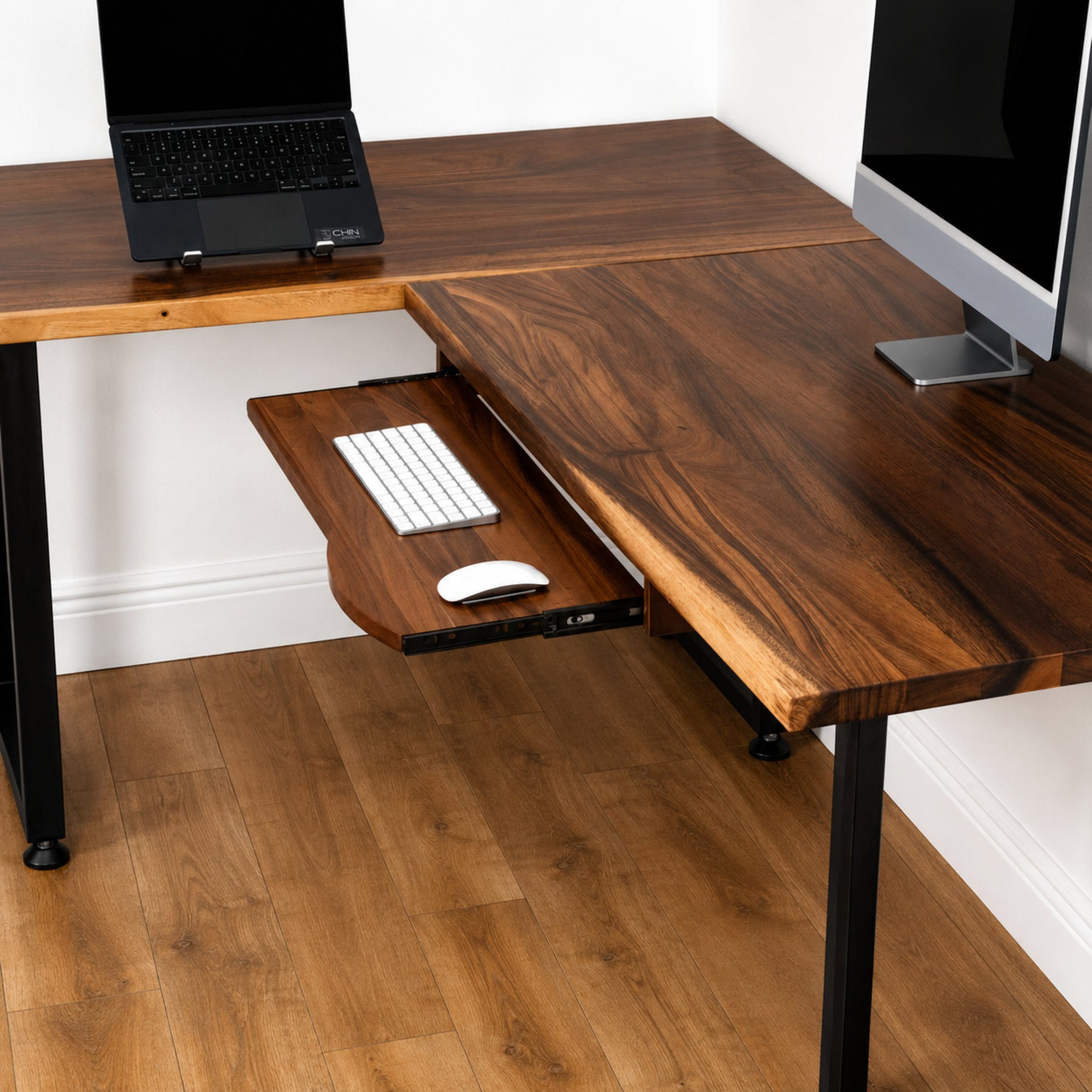 Walnut solid wood L-shaped desk with pull-out keyboard tray, laptop, and computer monitor.