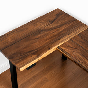 Walnut L-shaped standing desk with a black metal base on a wooden floor.