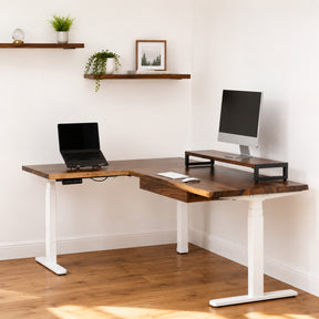 Walnut L-shaped standing desk with white legs in a home office setting.