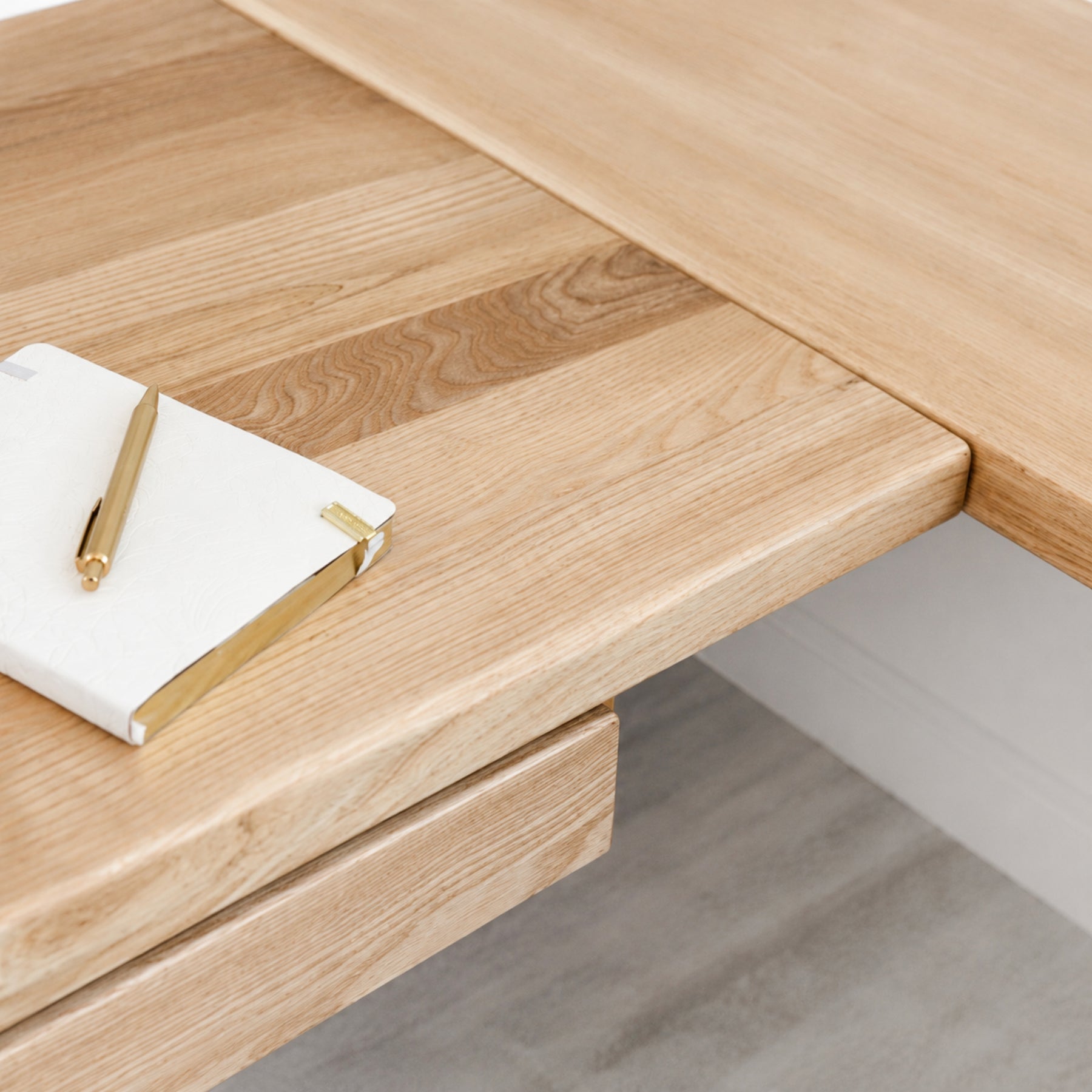 White oak L-shaped standing desk with a notebook and pen on top