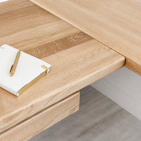 White oak L-shaped standing desk with a notebook and pen on top