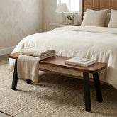 Bedroom bench with folded blanket and books in front of a bed with white bedding.