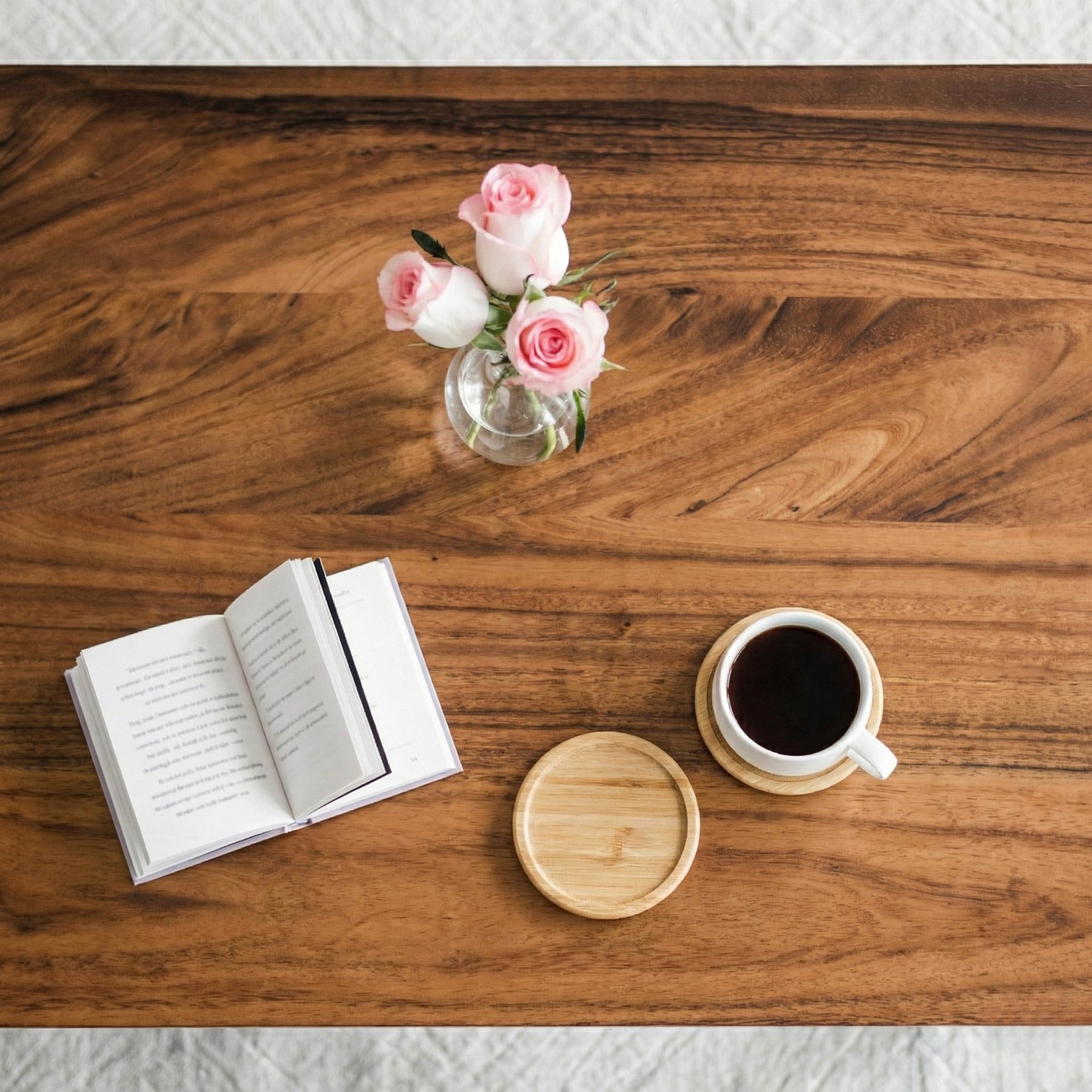 Open book, coffee cup, and vase with pink flowers on a walnut coffee table.