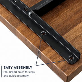 Close-up of a black dual-motor sit-stand frame attached to a wood-grain desktop, with text reading 'EASY ASSEMBLY' and arrows pointing to pre-drilled holes.