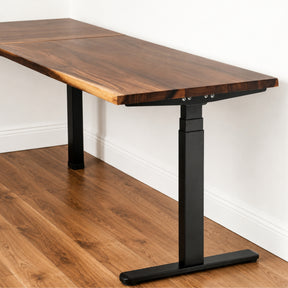 Walnut L-shaped standing desk with a black adjustable base on a wooden floor.