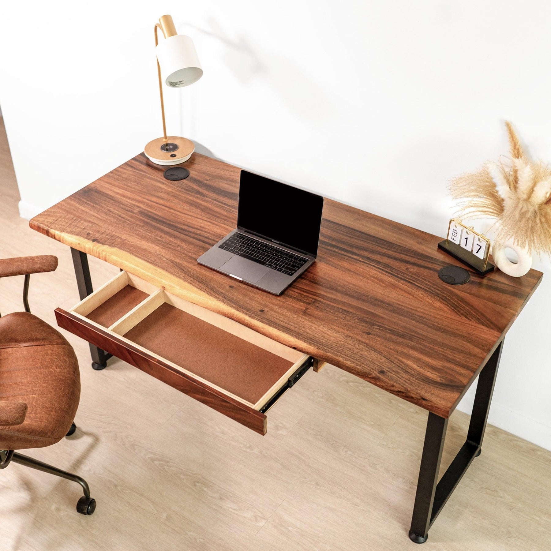 Overhead view of a stylish walnut solid wood computer desk with a live edge design, accompanied by a matching brown office chair, laptop, modern desk lamp, and minimalistic decor against a white wall.