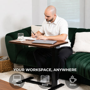 Man using an adjustable walnut laptop desk beside a sofa as a mobile workspace for writing and computer work