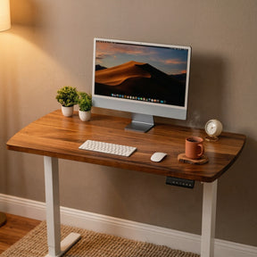 Narrow walnut standing desk with computer setup against a beige wall