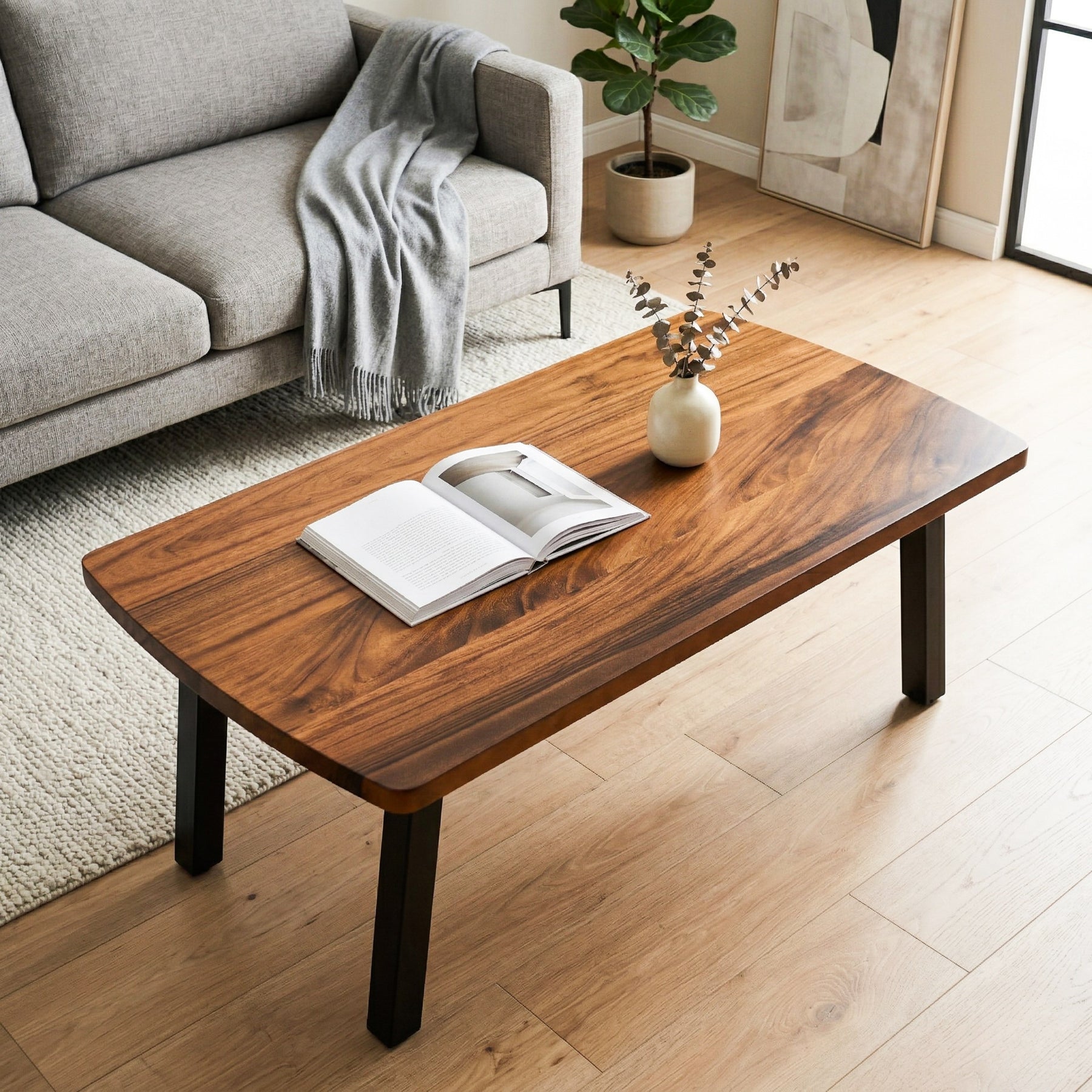 Walnut coffee table with an open book and a vase in a living room setting.