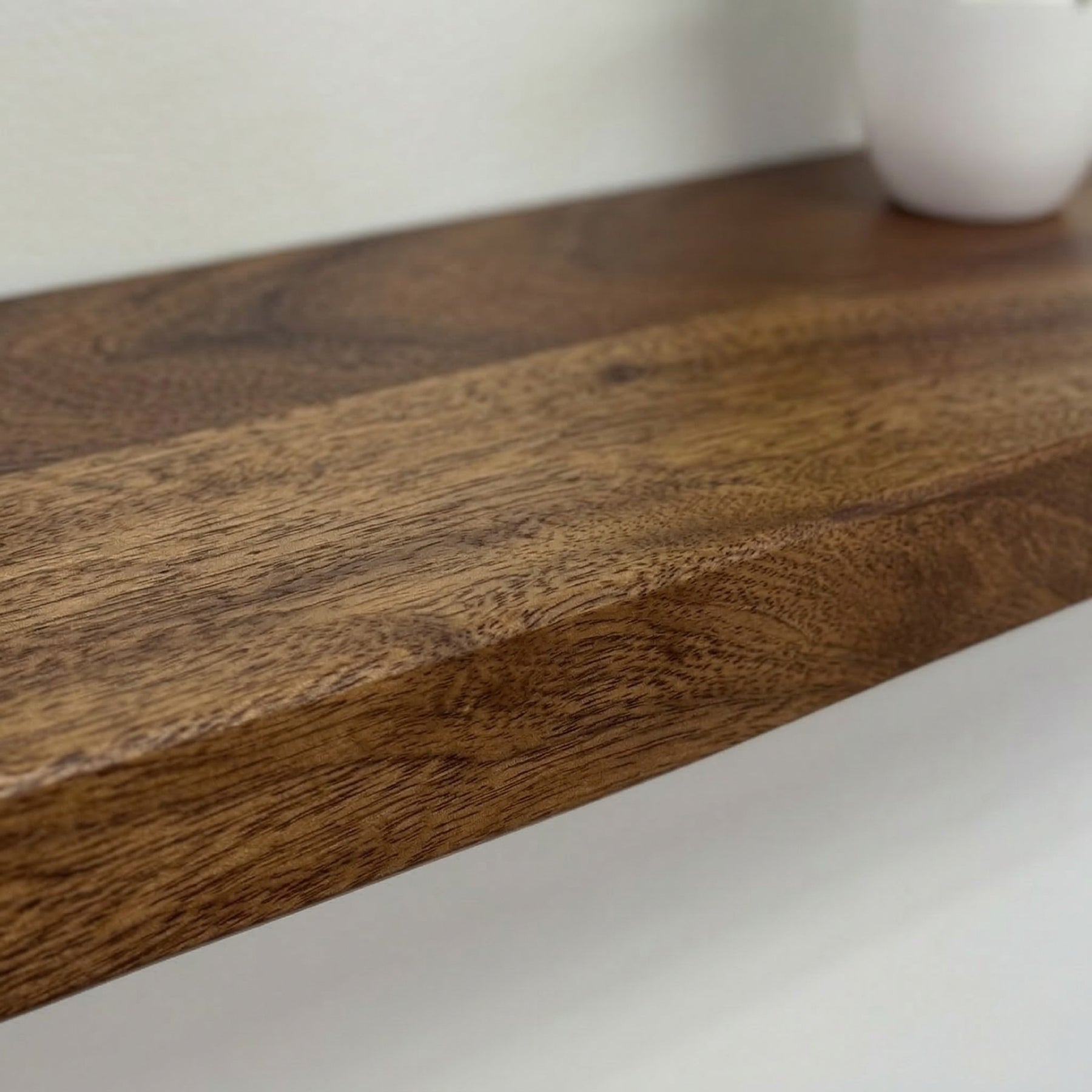 Close-up of a walnut shelf surface with a white vase in the background