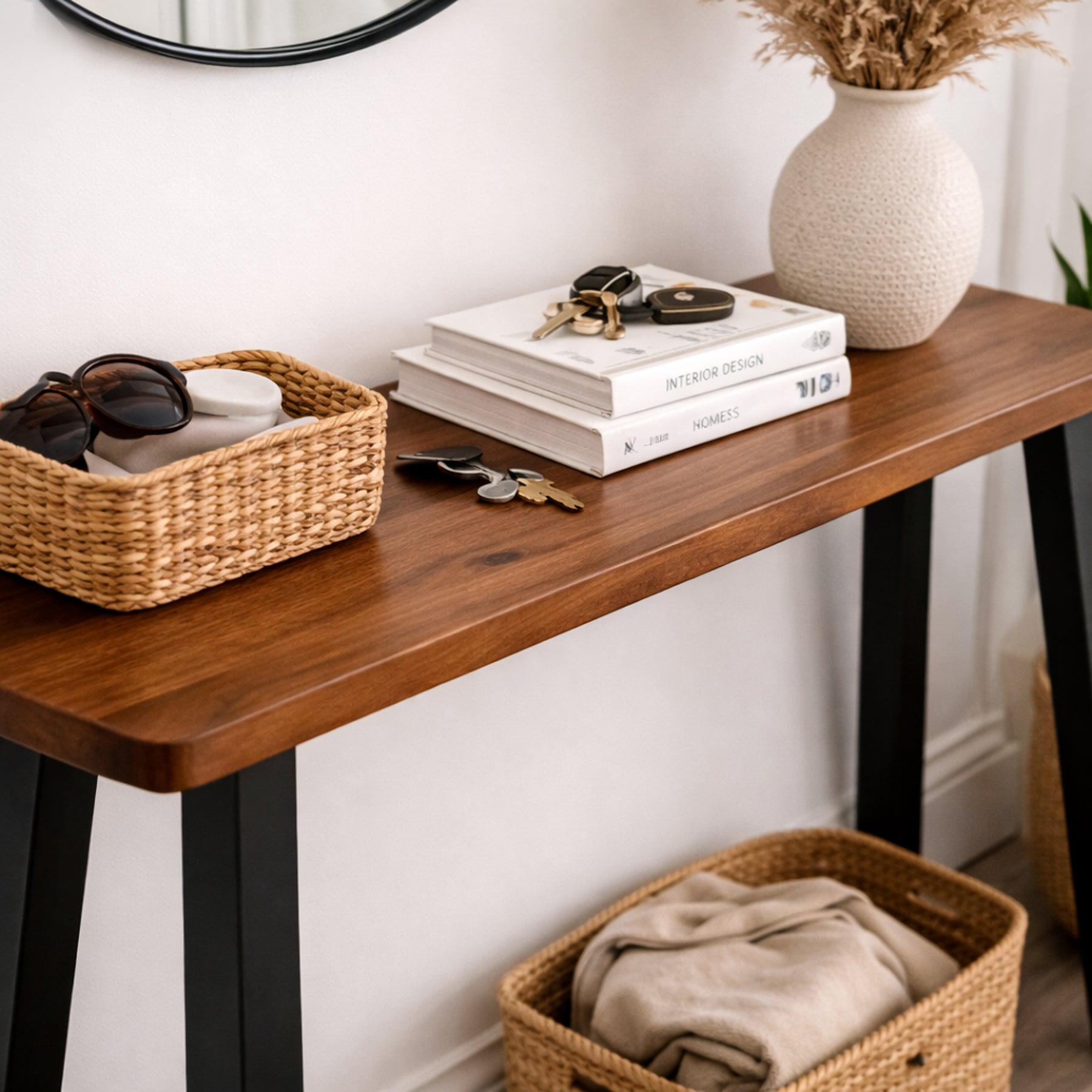 Walnut entryway console table with a basket, books, and a vase against a white wall.