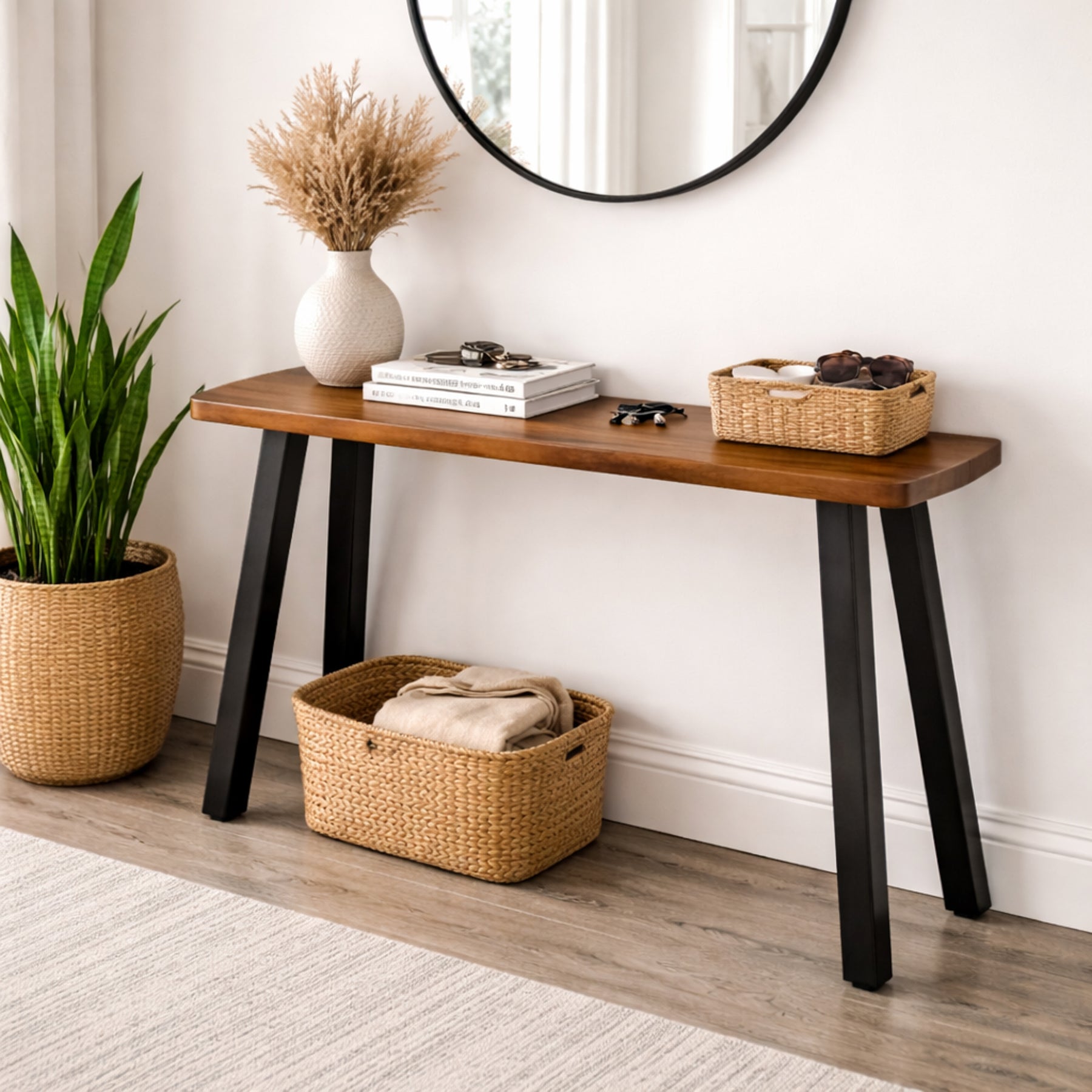 Walnut console table with black legs in a room with a plant and baskets.