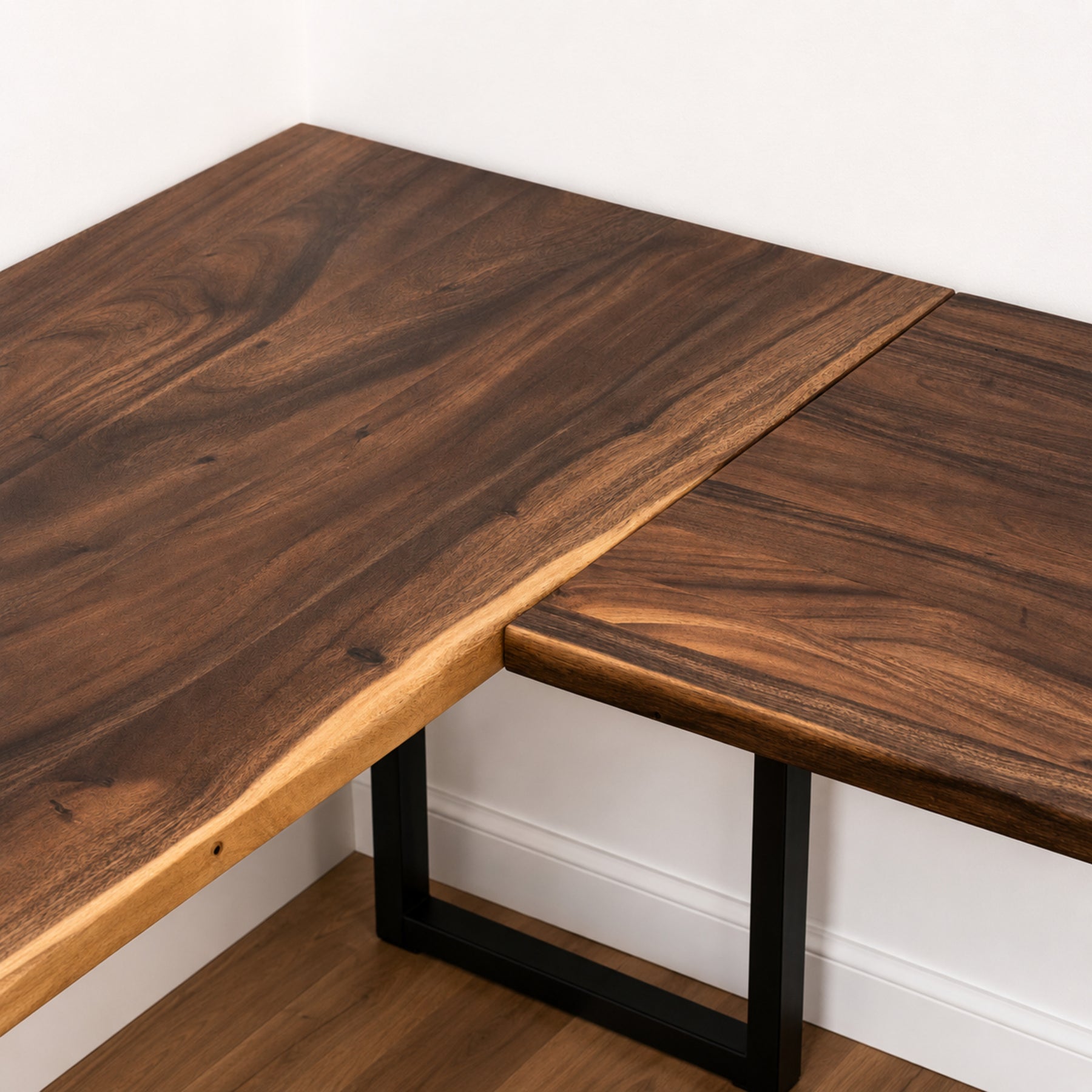 Walnut solid wood L-shaped desk with black metal legs against a white wall.