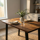 Compact solid walnut dining table set with plates, glasses, and a vase of greenery in a kitchen.