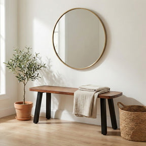 Wooden bench with a plant and basket in a room with a round mirror on the wall.