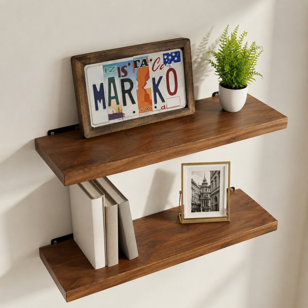 Walnut floating shelves with books, a framed picture, and a plant on a white wall.