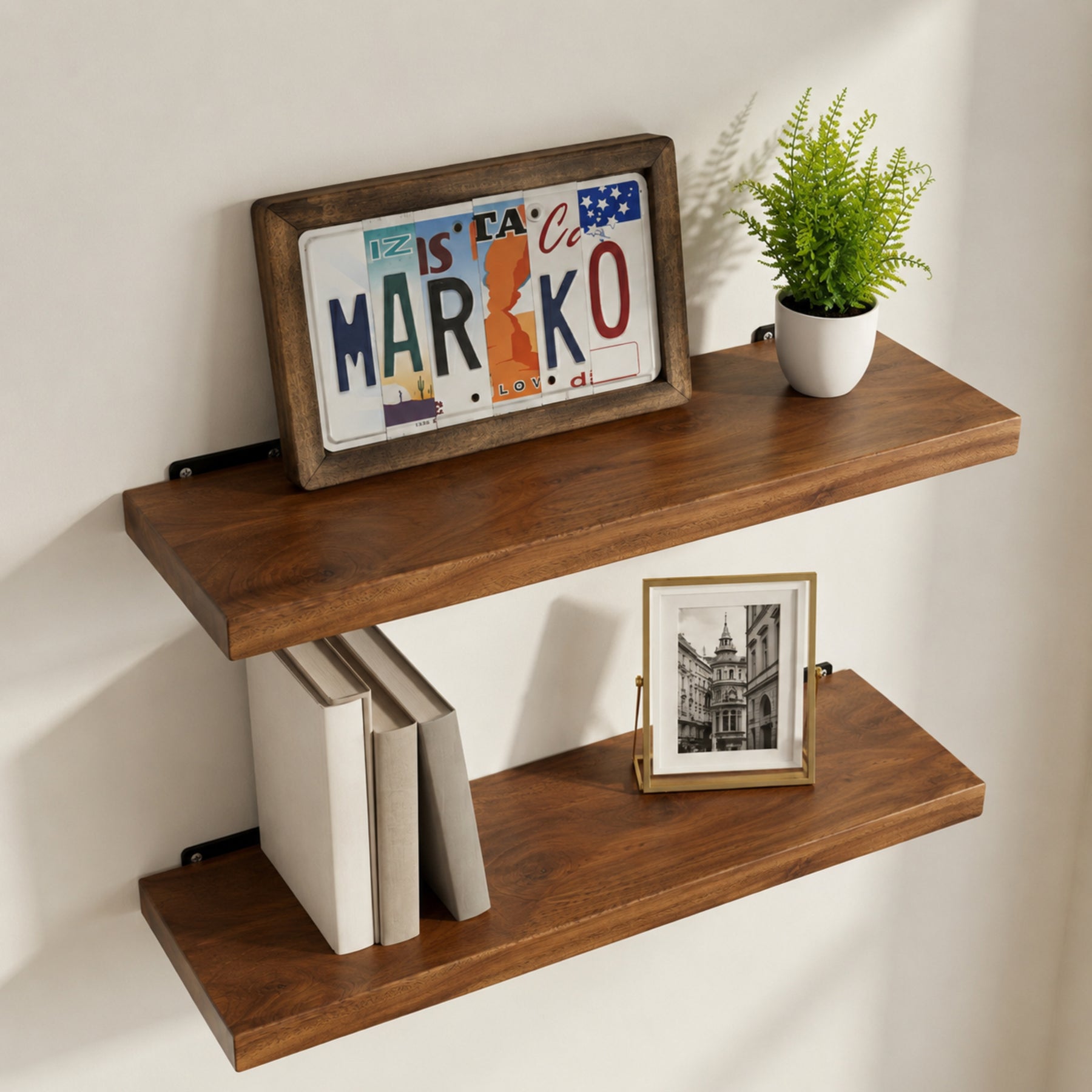 Walnut floating shelves with books, a framed picture, and a plant on a white wall.