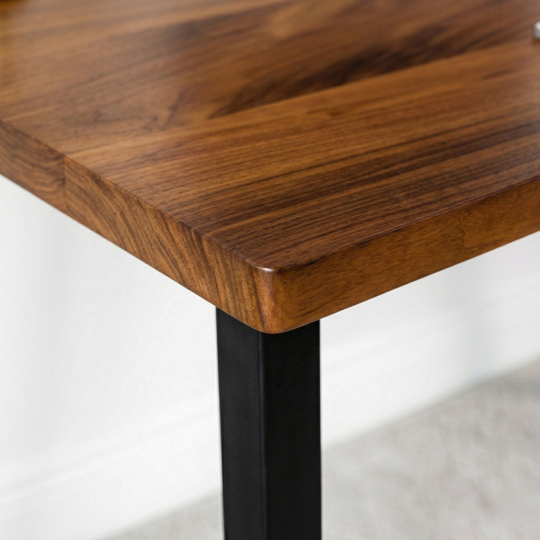 Close-up of a walnut desk with a black metal leg on a light gray background