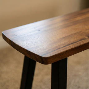 Solid wood bench with a dark brown top and black legs on a blurred background
