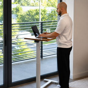 Person working while standing at a height-adjustable white oak mobile laptop desk