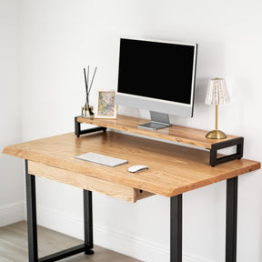 White oak computer desk with a drawer, desk with a computer setup against a white wall
