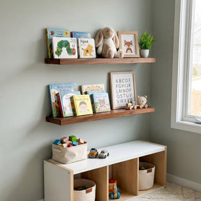 Wooden floating shelves with children's books, toys, and a teddy bear against a light gray wall.