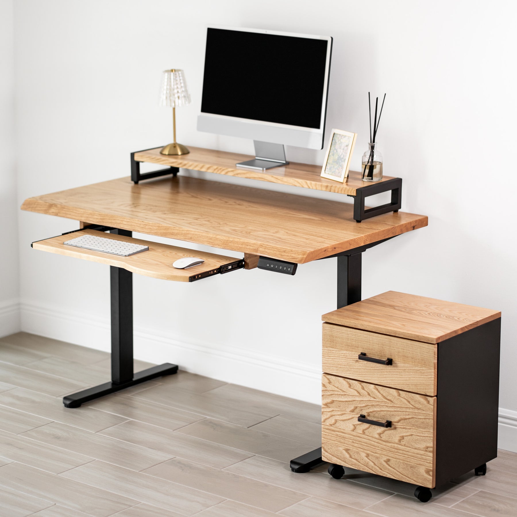 White oak standing desk with keyboard tray, computer setup, and file cabinet in a room.
