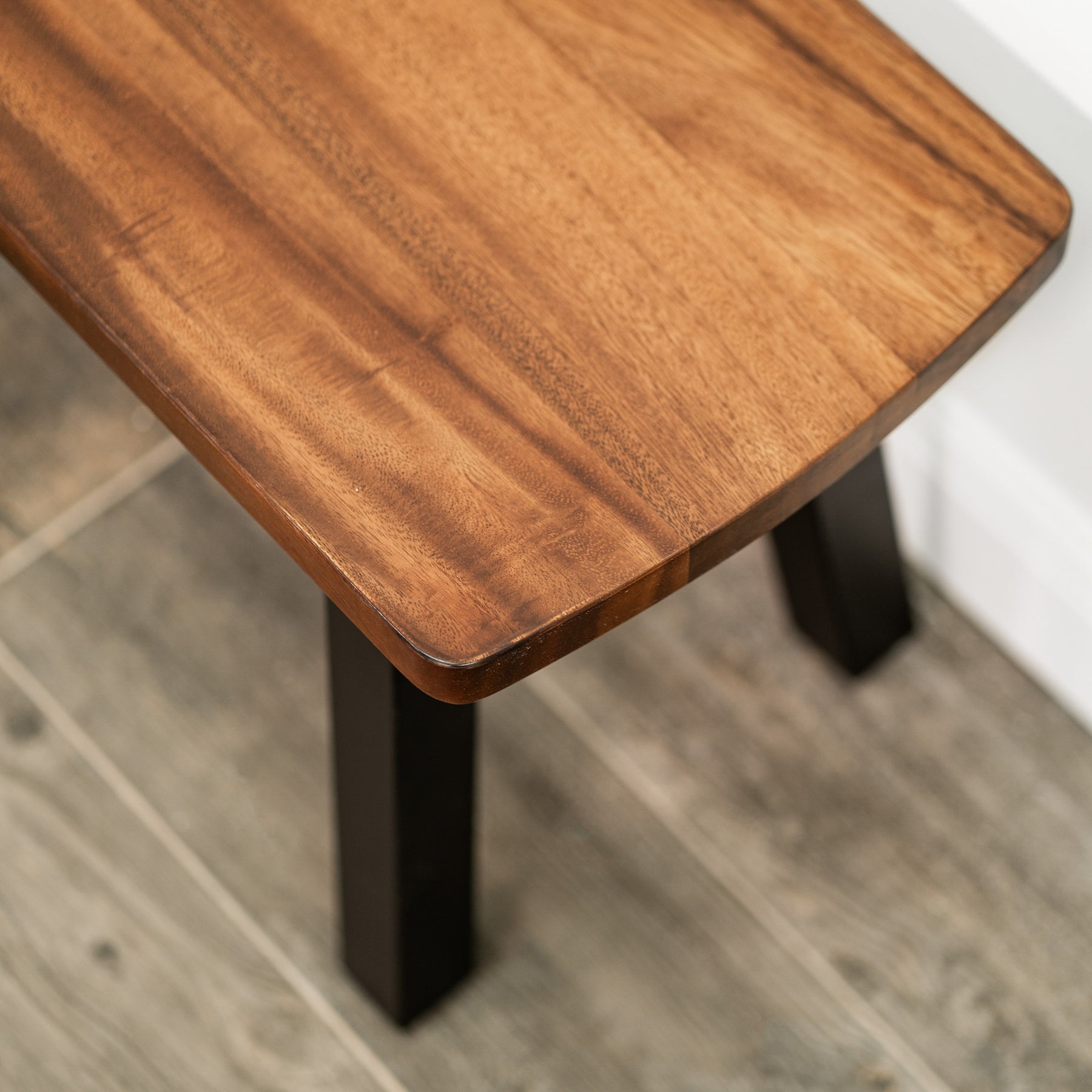 Solid walnut bench with black legs on a wooden floor